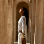 Model wearing an Ivory cape and matching sarong outfit standing in a sunlit archway of a beige building