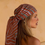 Model wearing a coral print headscarf against a beige background. Scarf dimensions: 208cm x 45cm