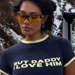 Model wearing a navy t-shirt with 'But Daddy I Love Him' text, standing outdoors. Wearing sporty sunglasses.