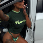 Model wearing a green 'Play Tech' shirt sitting in a vehicle while smoking a cigarette.
