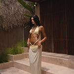 Model wearing a yellow swimsuit and matching sheer maxi skirt near a textured wall and standing on steps