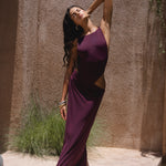 Model in a purple swimsuit posing near a textured wall.