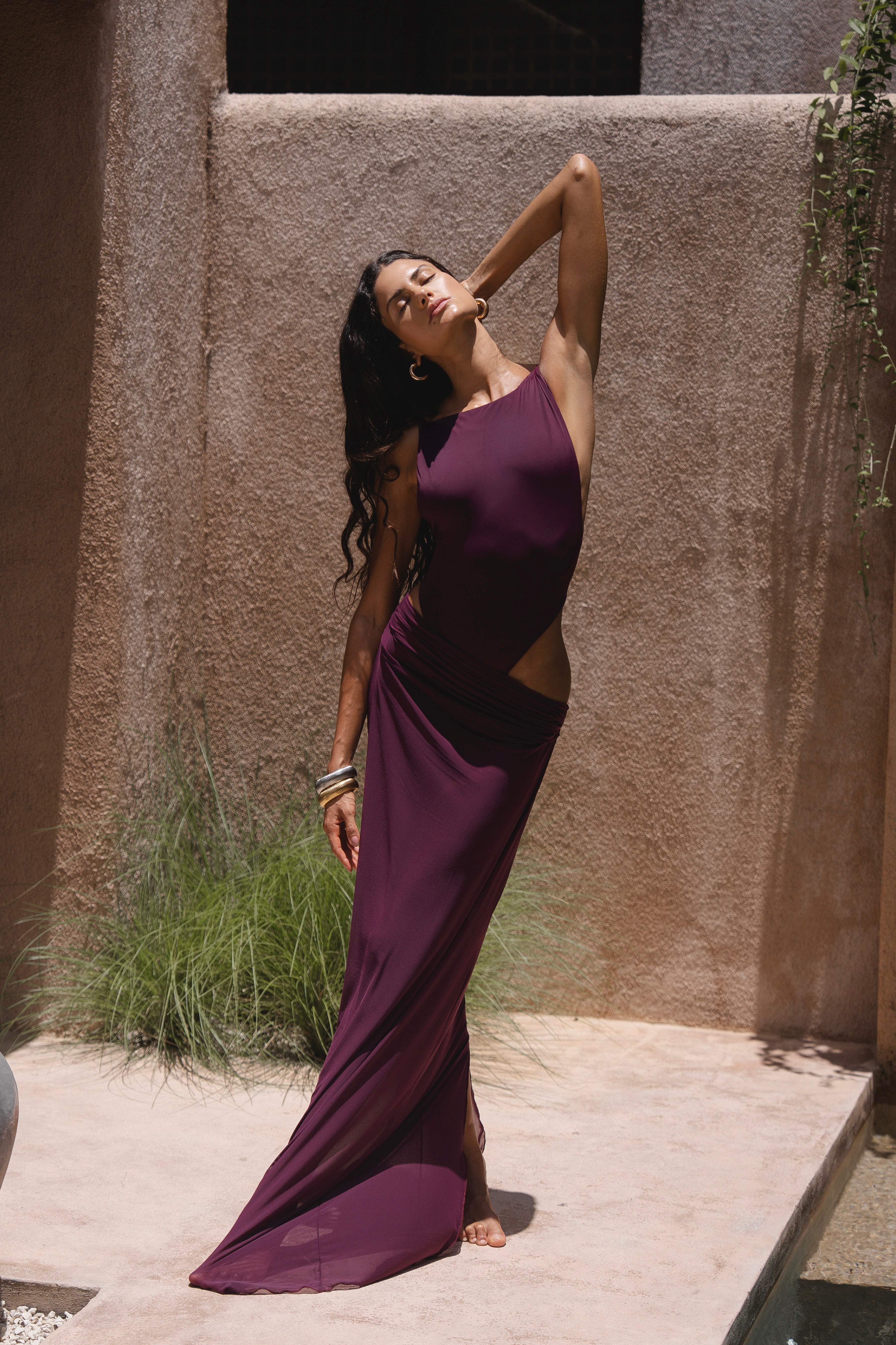 Model in a purple swimsuit posing near a textured wall.