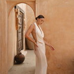 Side shot of model in a white dress standing in a sunlit archway with a warm-toned wall.