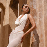 Side angle shot of model wearing an Ivory Maxi halter dress leaning against a neutral wall.