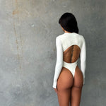 Back shot of model wearing a white long sleeve zip up one piece swimsuit in a studio.