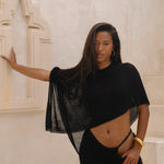 Model wearing a black sarong and black matching cape, posing in front of a neutral background