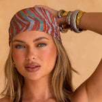 Model wearing a coral print headscarf against a beige background. Scarf dimensions: 208cm x 45cm