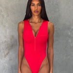 Close up shot of model in a red one piece zip up swimsuit  standing in front of a grey wall.