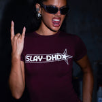 Model posing in a burgundy short-sleeve t-shirt with a white 'SLAY-DHD' graphic on the chest, paired with matching burgundy shorts, set against a dark textured background.