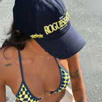 Model wearing a checkered bikini in Navy and Yellow and 'ROGUESEASON' branded cap standing on a street 