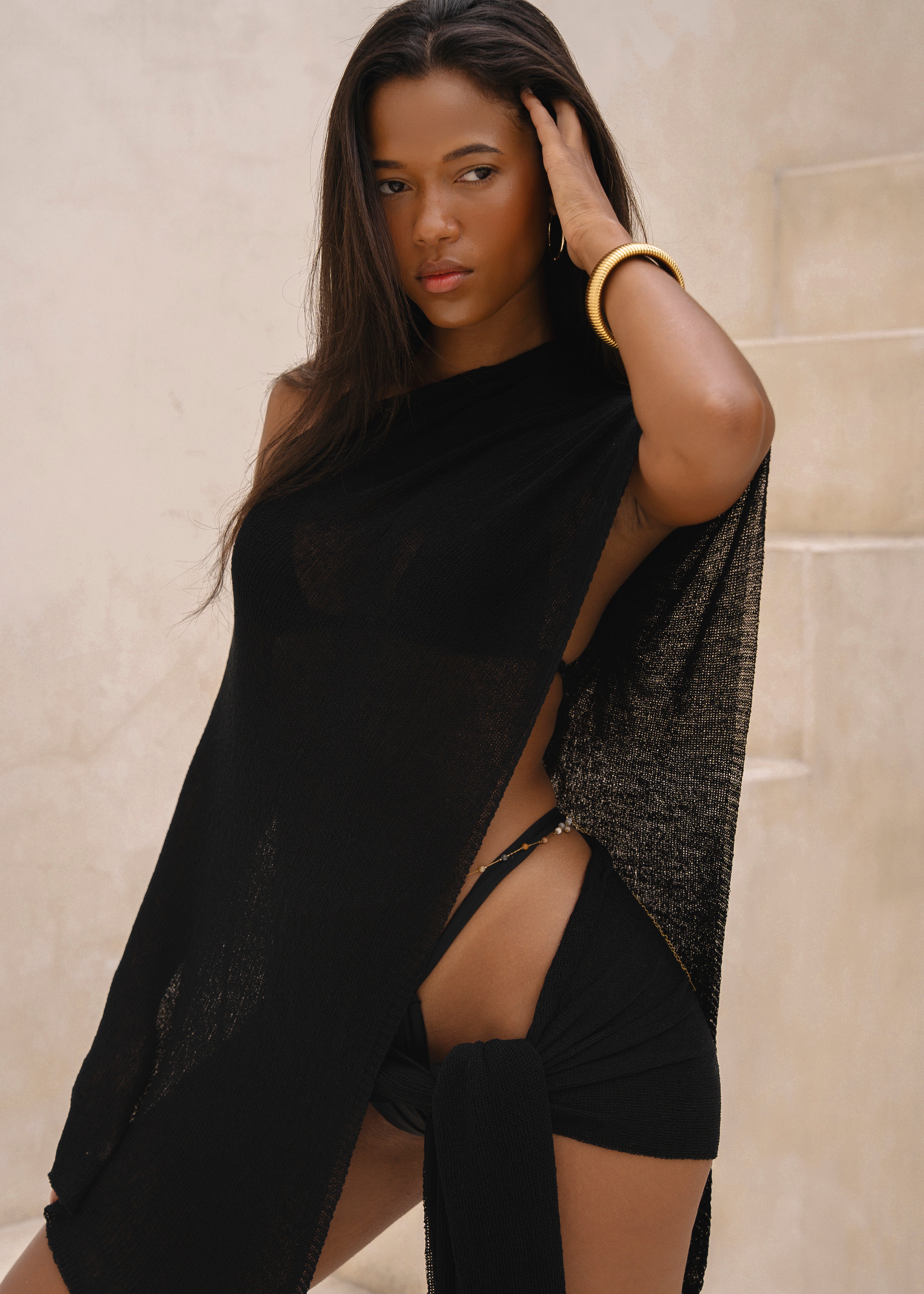 Model wearing a black sarong and black matching cape, posing in front of a neutral background