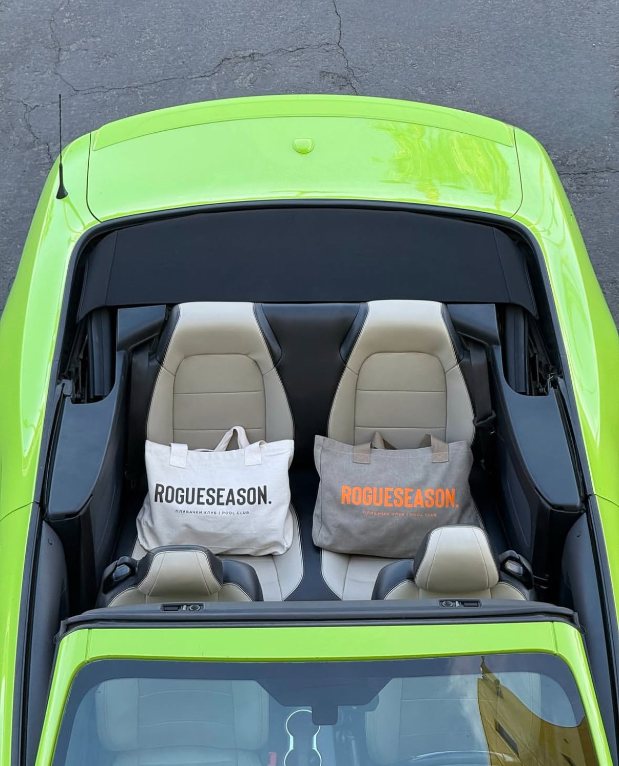 A grey and ivory canvas tote bag with the text 'ROGUESEASON' and 'плибач клуб' printed on them. The bags are placed on the back of a convertible car with the image taken from a high angle looking down at the car.