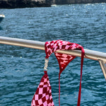 Red checkered bikini bottom placed on a yacht rail with the ocean in the background.