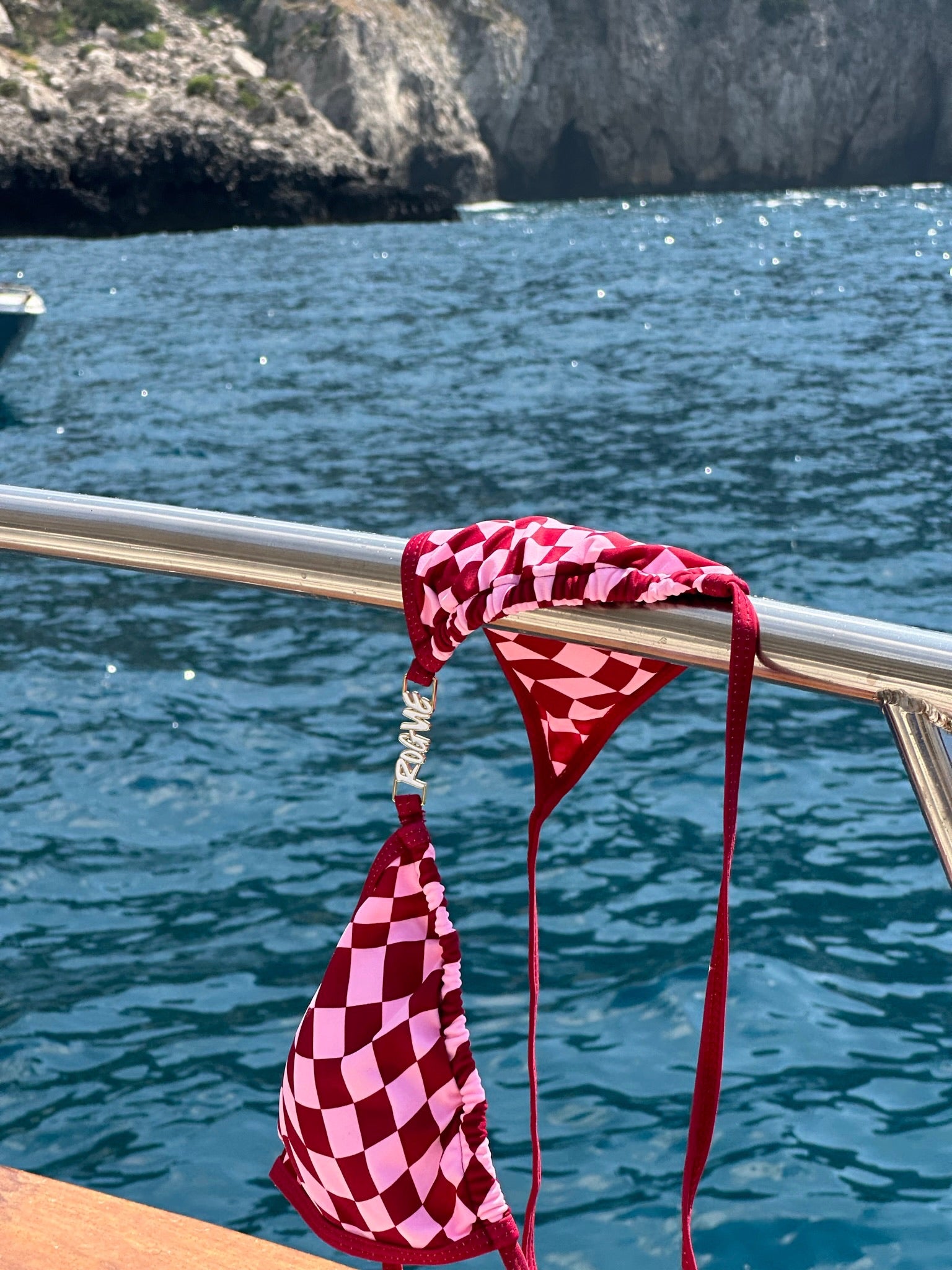 Red checkered bikini bottom placed on a yacht rail with the ocean in the background.