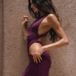 Model in a purple dress posing against a textured wall