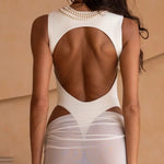 Close up back shot of model wearing an ivory bodysuit with a matching sheer maxi skirt with a fitted silhouette, standing indoors against a neutral-toned wall with minimal decor.