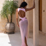 Back shot of model wearing a pink one-piece swimsuit featuring a cut out open-back design and high-cut leg. styled with a sheer maxi skirt. Photographed against a warm textured backdrop, outdoors , highlighting the swimsuit's elegant silhouette and modern resortwear aesthetic.