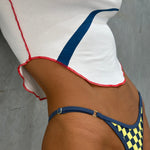 Close up detail shot of model wearing a white tee and a yellow and navy checkered bikini bottom leaning on a grey wall.
