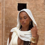 Model wearing sarong as headscarf with a gold bracelet against a beige wall.