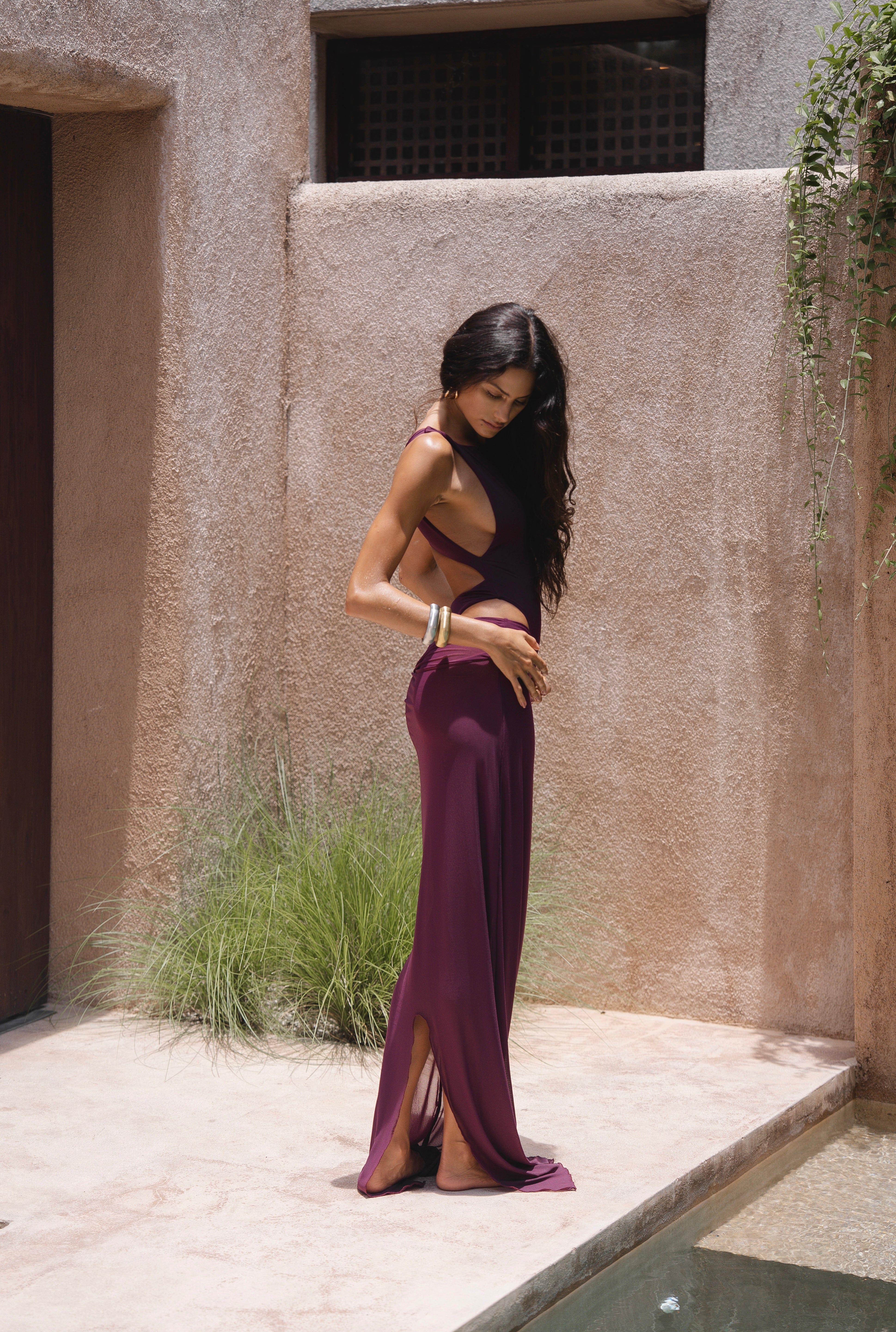 Model wearing a burgundy swimsuit and matching sheer maxi skirt near pool with a textured wall