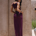 Back shot of model in a purple swimsuit standing near a textured wall.