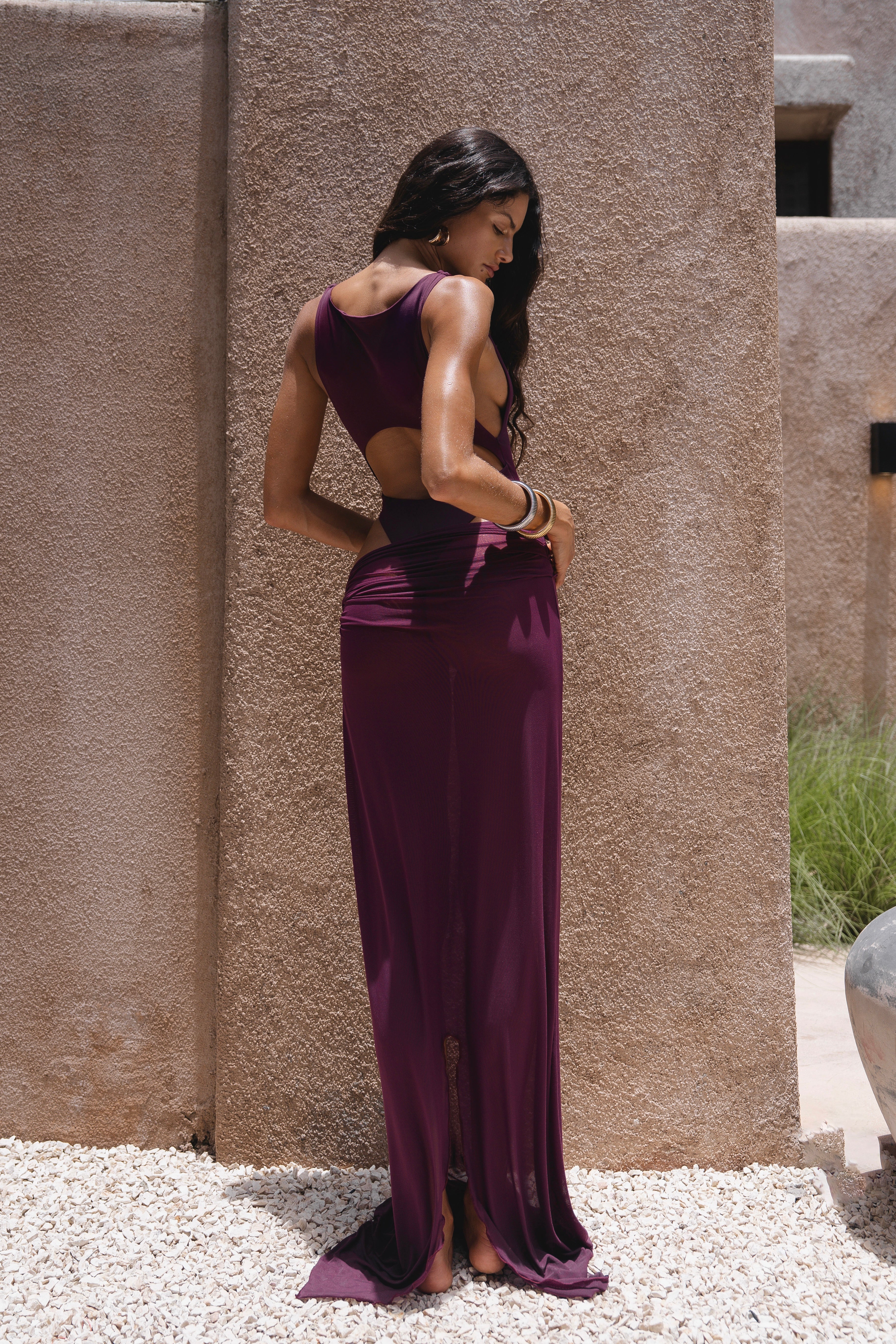 Back shot of model in a purple swimsuit standing near a textured wall.