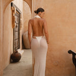 Back shot of model wearing Ivory maxi halter dress with neutral rustic background.