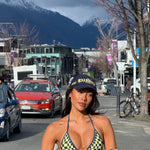 Model wearing a checkered bikini in Navy and Yellow and 'ROGUESEASON' branded cap standing on a street with mountains in the background