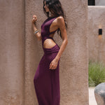 Side shot of model wearing a burgundy swimsuit and matching sheer maxi skirt near a textured wall