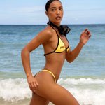 Model in Rogue Season yellow and black bikini running on a beach with ocean waves in the background