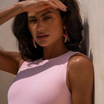 Close up shot of model covering her face from the sun while wearing a pink swimsuit and statement earrings.