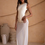 Side shot of model wearing an ivory bodysuit with a matching sheer maxi skirt with a fitted silhouette, standing indoors against a neutral-toned wall with minimal decor.