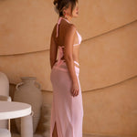 Model wears a soft pink halter bikini paired with a matching sheer maxi sarong. The styling creates a feminine, elevated vacation-inspired aesthetic.