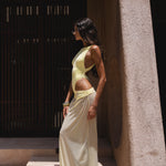 Model in a yellow swimsuit and matching sheer maxi skirt standing on steps with a building in the background