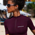 Close up shot of model wearing a short-sleeve burgundy zip-up Swim top on a beach.