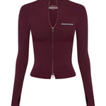 A long-sleeve, fitted zip-up jacket in deep burgundy, featuring a high mock neck, a front zipper, and blue text branding on the chest, displayed on a solid white background.
